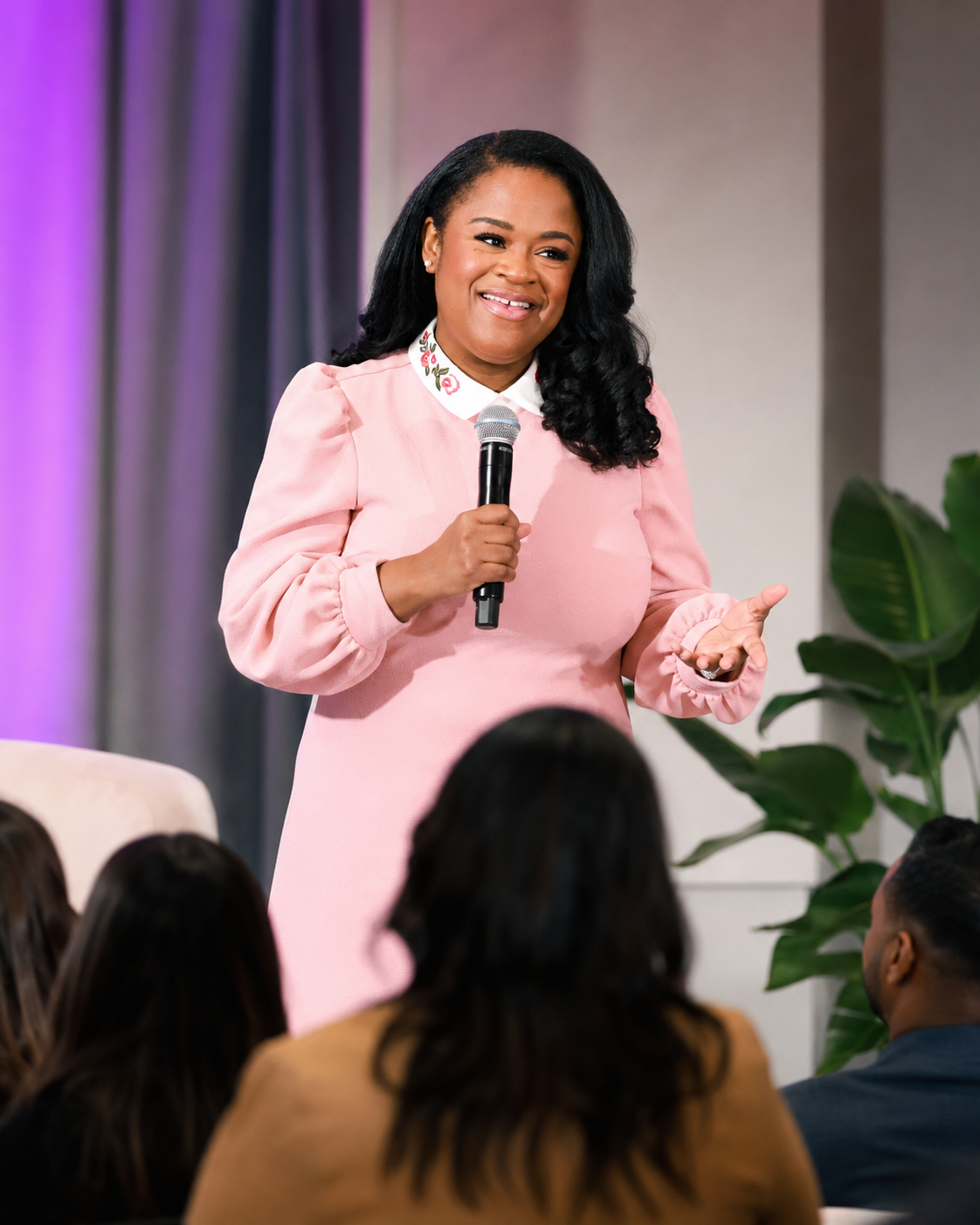 Alicia Perkins speaking on stage with a microphone to a seated audience